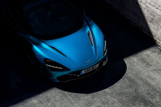 The front of a blue sportscar emerging from shadow.