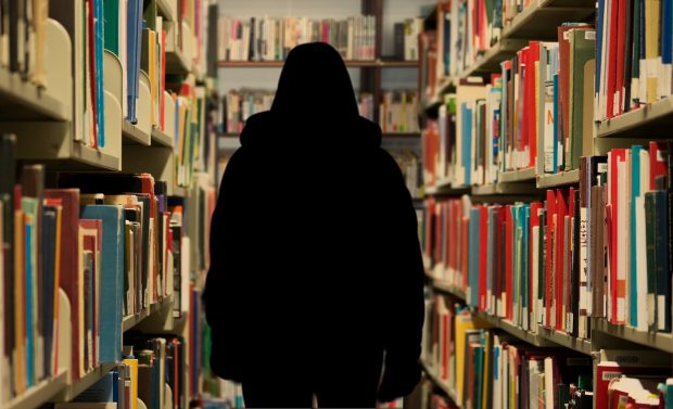 Anonymous figure standing between bookshelves.