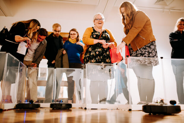 People looking at small robots on the floor.