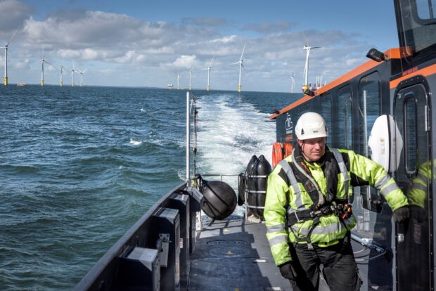 Man in high visibility clothing on a boat in front of an offshore wind farm.